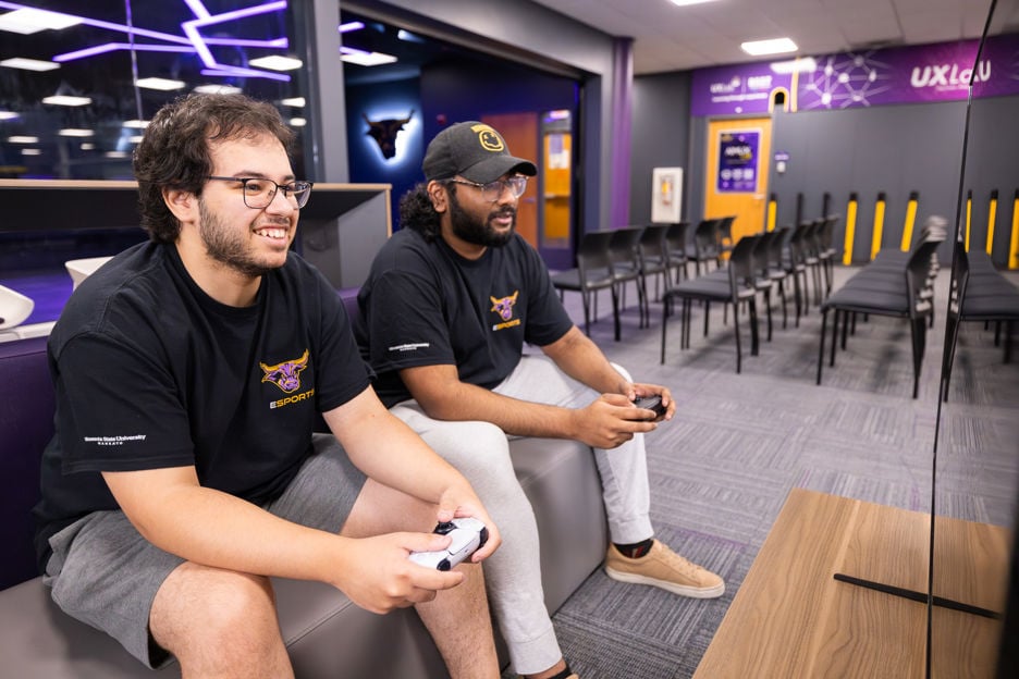 Two students sitting on a couch in the Esports room playing a game on the Playstation Switch