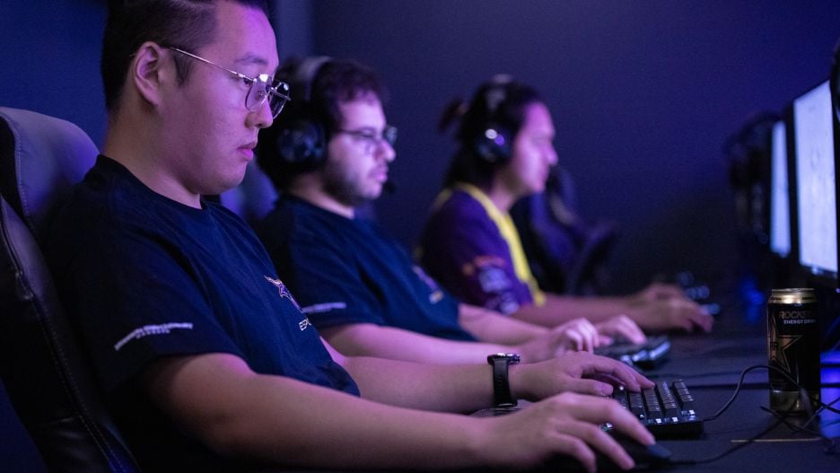 A row of student gamers gaming on PCs in a dark gaming facility.
