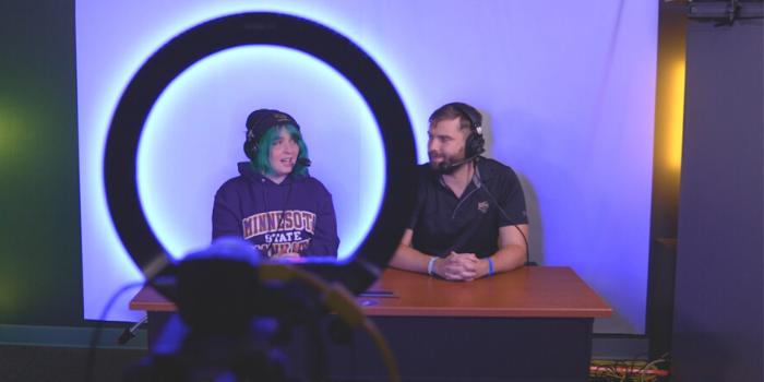Photo of two esports students shoutcasting on a livestream in the esports broadcast studio set.