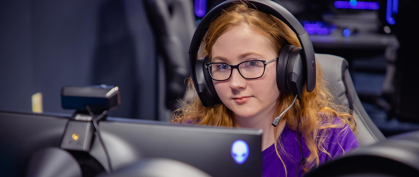 Girl wearing headphones and gaming on a PC, smiling at the camera