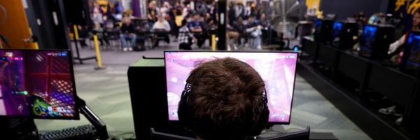 Up close photo of a student competing in Kato Clash, gaming on a large PC screen, while a crowd watches from beyond.